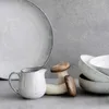 A still life arrangement of ceramic tableware and mushrooms on a gray surface. Produktbild-Vorschau
