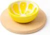 A yellow bowl shaped like a lemon slice sits on a round wooden board. Anteprima dell’immagine prodotto