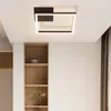 A modern square LED ceiling light fixture is mounted on a white ceiling above a built-in wooden shelving unit. Voir les images du produit