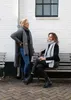 Two women wearing scarves and cardigans, sitting and standing next to a white brick wall. Produktbild-Vorschau
