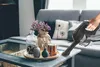 A hand is using a cordless vacuum cleaner to clean a coffee table in a living room. Voir les images du produit
