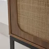 A close-up view of a cabinet with a rattan weave door and wood-effect frame, resting on black metal legs. Produktbild-Vorschau