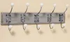 A coat rack with five hooks mounted on a wooden board against a plain wall. Produktbild-Vorschau