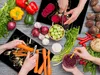 A top-down view of a kitchen scene with various vegetables and hands preparing them. Náhľad obrázku produktu