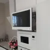 A white smart TV is mounted above a white microwave in a modern kitchen. Produktbild-Vorschau