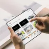 A person is holding a tablet displaying YouTube videos, with a book in the background. Náhled obrázku produktu