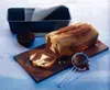 A marble cake is sliced and placed on a wooden board next to a baking pan and a small bowl of cocoa powder. Podgląd zdjęcia produktu