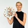 A woman is holding a clock with a cat illustration on it. Produktbild-Vorschau
