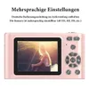 A pink digital camera is shown from the back, displaying a photo of a woman sitting by a body of water with the sun setting behind her. Text above the camera describes its multilingual settings. Produktbild-Vorschau
