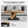 A modern coffee table with a wooden top and a dark base, placed in a living room setting with a sofa in the background. A weight is placed on the table to demonstrate its sturdiness. Produktbild-Vorschau