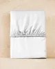 A white fitted sheet is folded and placed on a light wooden surface. Produktbild-Vorschau