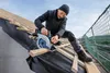 A man is working on a roof, using a circular saw to cut wooden planks. Produktbild-Vorschau