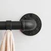 A close-up view of a black metal pipe fitting attached to a wall, with a black pipe extending horizontally and a light-colored fabric item hanging from it. Produktbild-Vorschau