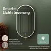 A modern oval mirror with integrated LED lighting is displayed against a dark green wall, with text overlays explaining its smart lighting features. Produktbild-Vorschau