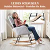 A woman is sitting in a rocking chair and reading a book. Produktbild-Vorschau