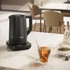 A black Haier electric kettle is shown on a countertop next to a cup of tea and tea leaves. Podgląd zdjęcia produktu
