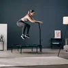 A woman is jumping on a fitness trampoline in a living room. Voir les images du produit