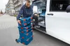 A man is loading a stack of blue toolboxes onto a dolly next to a white van. Podgląd zdjęcia produktu