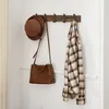 A wooden coat rack mounted on a white wall, with a hat and a plaid shirt hanging on it. Produktbild-Vorschau