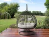 A hanging egg chair for two people is placed on a wooden deck in a garden setting. Náhled obrázku produktu