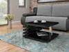A modern living room scene with a black high-gloss coffee table in the foreground, a gray sofa in the background, and a vase of flowers to the left. Náhled obrázku produktu
