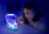 A young girl is looking intently at a glowing, illuminated aquarium with tiny creatures inside. Voir les images du produit