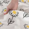 A hand is shown pressing down on a white fabric with a black and yellow daisy pattern. Produktbild-Vorschau