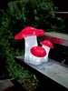 Three illuminated mushroom decorations are placed on wooden steps, with a dark green evergreen bush in the background. Produktbild-Vorschau