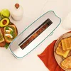 A toaster with toast inside, placed on a table with some breakfast items like avocado toast, an apple, and a bottle. Voir les images du produit