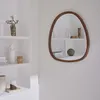 A mirror with a wooden frame hangs on a white wall next to a white shelving unit with various decorative items. Produktbild-Vorschau