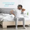 A man sitting on a bed, holding his back and neck in pain. Produktbild-Vorschau