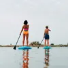 Two people paddleboarding on a calm body of water under an overcast sky. Podgląd zdjęcia produktu