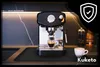 An espresso machine is shown on a kitchen counter with a protective mat underneath. There is a cup of espresso being brewed and another cup of coffee on the side. Náhled obrázku produktu