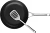 A top-down view of a black frying pan with a silver spatula resting inside it. Produktbild-Vorschau