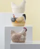Three ceramic chicken-shaped containers are displayed on white shelves against a light yellow background. Náhled obrázku produktu