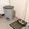 A gray pedal trash can with a dark gray lid and a broom on a mat. Náhled obrázku produktu