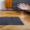 A dark gray shaggy rug is placed on a wooden floor in front of a mid-century modern wooden cabinet. A hand is shown pressing into the rug, highlighting its softness. Anteprima dell’immagine prodotto