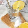 A glass of water with a lemon slice and a spoon, next to a pile of white powder and more lemon slices on a wooden board. Produktbild-Vorschau