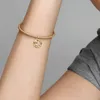 A close-up of a person's arm wearing a gold bracelet with a charm. Voir les images du produit