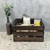 A wooden crate filled with painting supplies, including jars of paint and brushes, placed on a speckled surface with a gray textured wall in the background. Produktbild-Vorschau