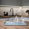 A kitchen counter with a dish drying mat holding glasses and wine glasses. The background shows a modern kitchen with a sink and cabinets. Podgląd zdjęcia produktu