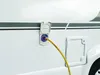 A yellow hose is plugged into a blue and white connector on the side of a white RV. Voir les images du produit