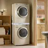 A stacked washer and dryer unit in a laundry room, with shelving and a doorway visible. Produktbild-Vorschau