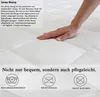 A hand resting on a white mattress cover with text overlays describing its features and care instructions. Produktbild-Vorschau