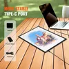 A light table with a drawing on it is placed on a wooden table next to a laptop and a power bank, suggesting portability and different power sources. Produktbild-Vorschau