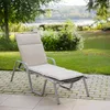 A chaise lounge with a beige cushion sits on a paved patio in a garden setting with trees and a body of water in the background. Produktbild-Vorschau