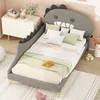 A child's bed with a dinosaur-shaped headboard, decorated with pillows and blankets, in a bedroom setting. Produktbild-Vorschau
