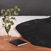 A black fitted sheet is laid out on a mattress, with a vase of flowers and a book on a wooden surface in the foreground. Anteprima dell’immagine prodotto