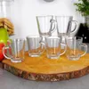 A set of six clear glass espresso cups arranged on a wooden board, with some fruit and cookies in the background. Voir les images du produit