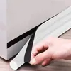 A hand is peeling off the backing of a white foam door seal with a black adhesive strip. Náhled obrázku produktu